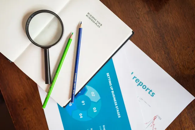 A top view of a magnifying glass, colored pencils, and business reports on a wooden table. Common science and health reporting problems