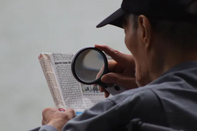 Elderly man using a magnifying glass to enhance text in a newspaper. Image and video verification checklist for the desk