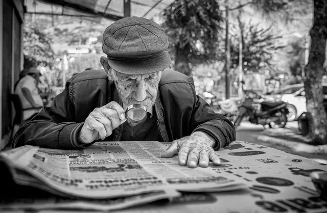 A senior man uses a magnifying glass to read a newspaper outdoors, highlighting aging and focus. Science and health news verification guide