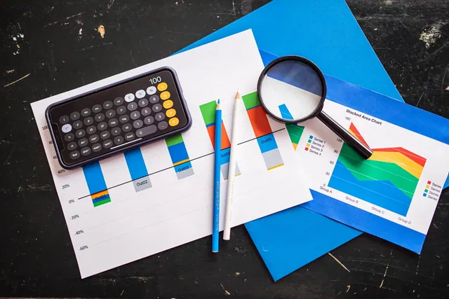 Top view of financial charts with a smartphone calculator, magnifying glass, and pencils on a desk. Statistics and chart verification checklist