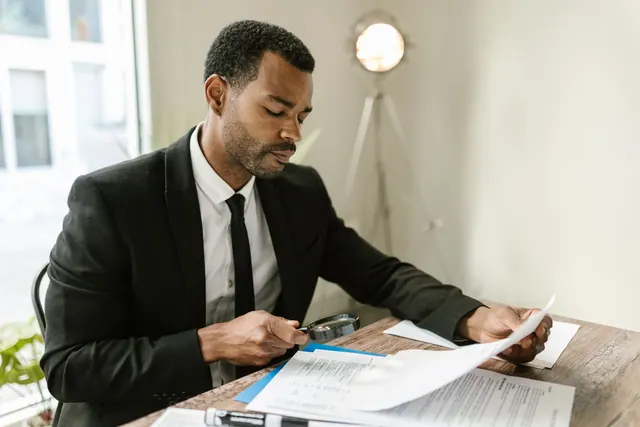 Professional man examines paperwork with magnifying glass at office desk, highlighting attention to detail. Visual verification methods compared, from reverse search to metadata